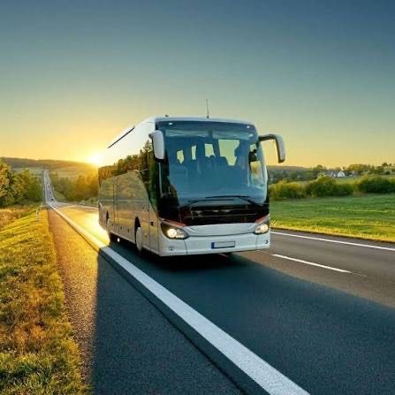 Ein großer Bus fährt auf einer zweispurigen Straße mit Gras auf beiden Seiten, und die Sonne geht im Hintergrund unter.