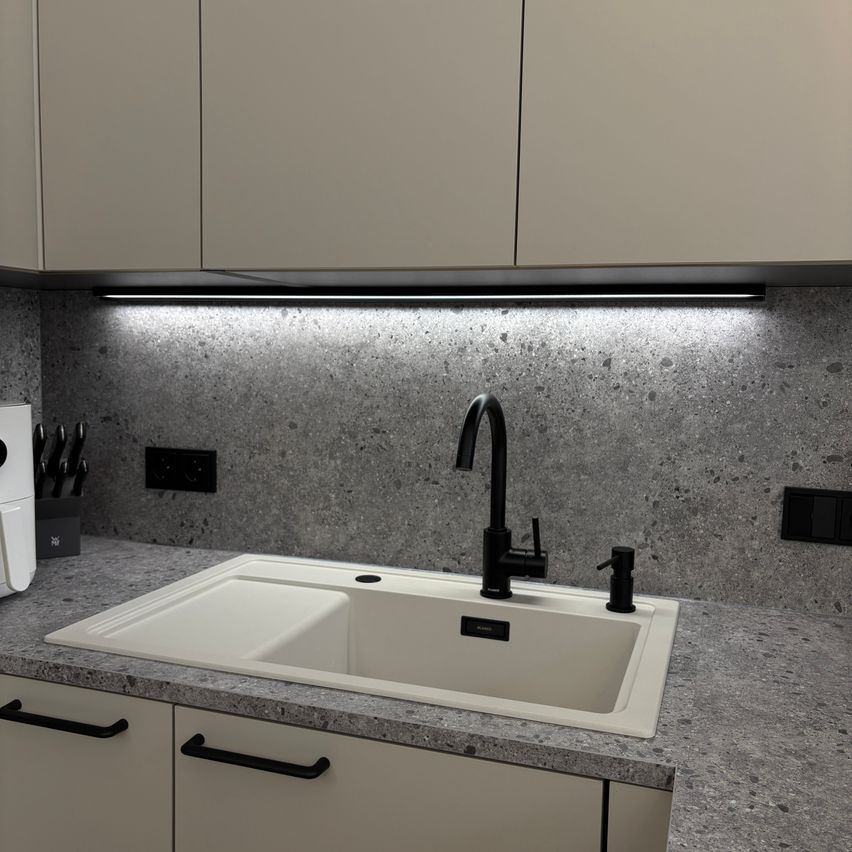 Eine moderne Küche mit Granitarbeitsplatten und einer weißen Spüle. Ein schwarzer Wasserhahn ist über der Spüle und ein weißes Gerät ist links.