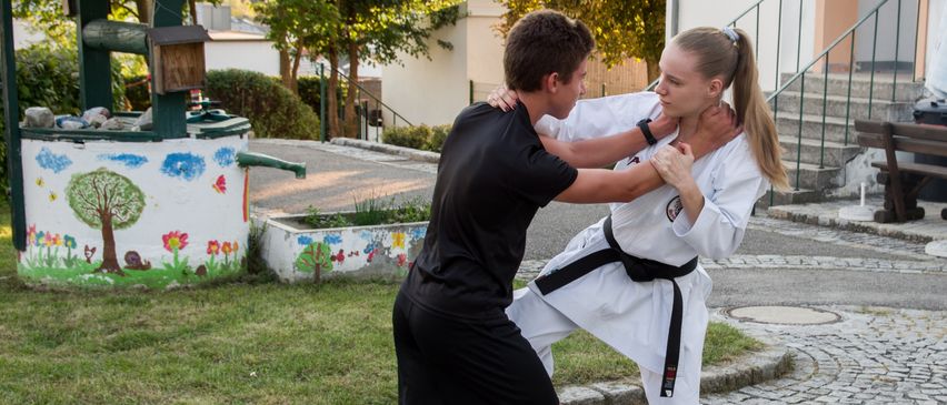 A young man and woman practicing karate on a cobblestone street. The woman is in a white gi, and the man in a black one.