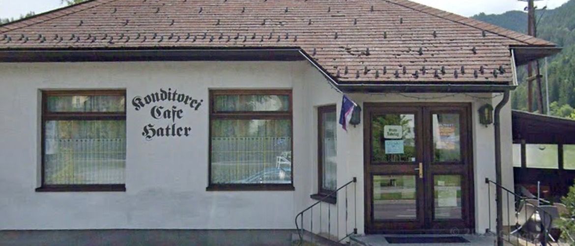 Ein kleines Café namens 'Rouditorci Cafe Satler' mit einem braunen Dach und einer Flagge davor, in einem Gebirgsgebiet gelegen.