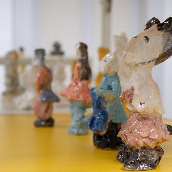 Nahaufnahme einer Gruppe von Keramikfiguren in verschiedenen Farben und Größen auf einem gelben Tisch.