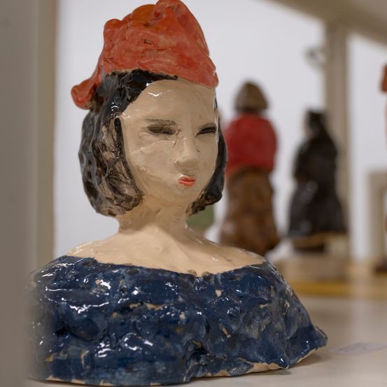 Ein Nahaufnahme einer Frauenbüste mit rotem Hut. Dahinter sind weitere Skulpturen zu sehen.