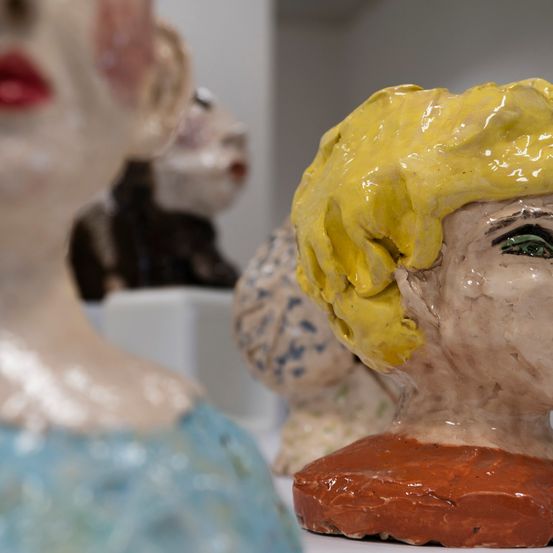 Nahaufnahme von drei Tonbüsten mit unterschiedlichen Farben und Texturen. Eine Büste hat blonde Haare, eine andere schwarze Haare und die dritte hat blaue und weiße Muster.
