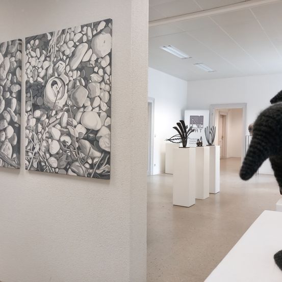 Ein Kunstgalerie mit zwei großen Schwarz-Weiß-Gemälden an der Wand und mehreren weißen Podesten mit Skulpturen in der Mitte.