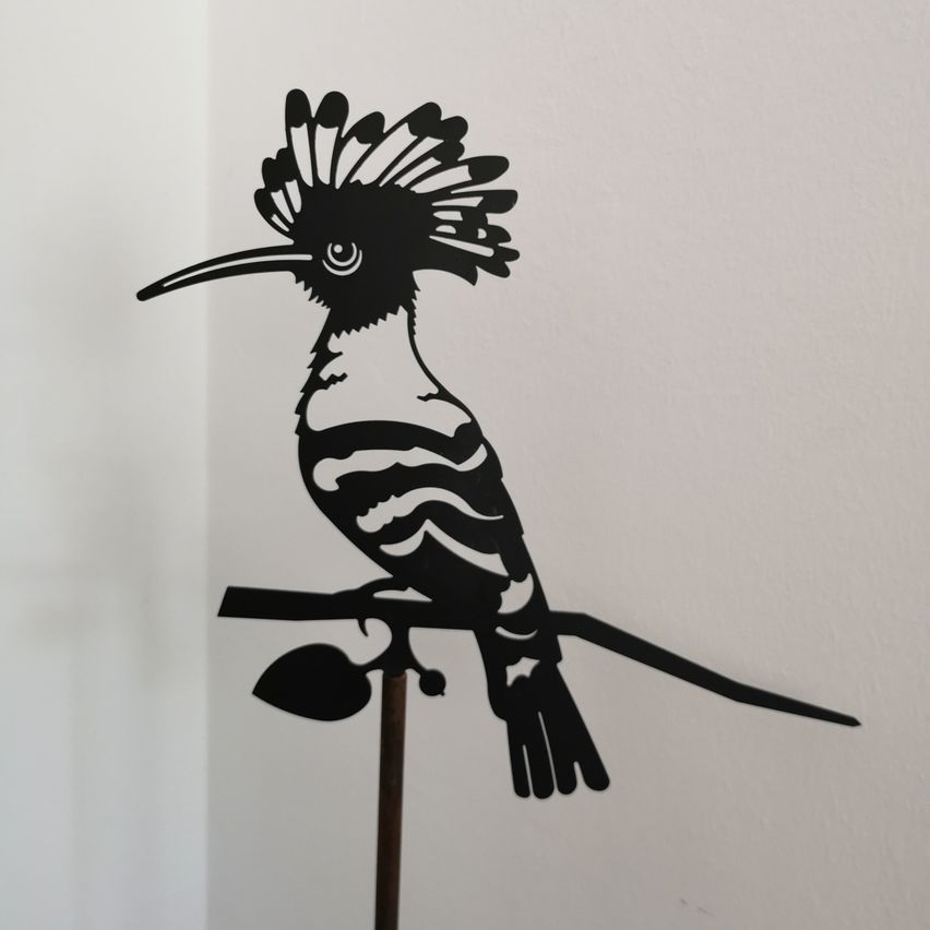 Eine Silhouette eines Vogels mit langem Schnabel, der auf einem Ast sitzt und an einer weißen Wand befestigt ist.