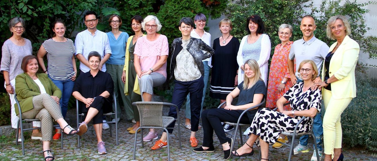Eine Gruppe von Erwachsenen, sowohl Männer als auch Frauen, posiert für ein Foto im Garten. Sie tragen alle Freizeitkleidung und einige tragen eine Brille.