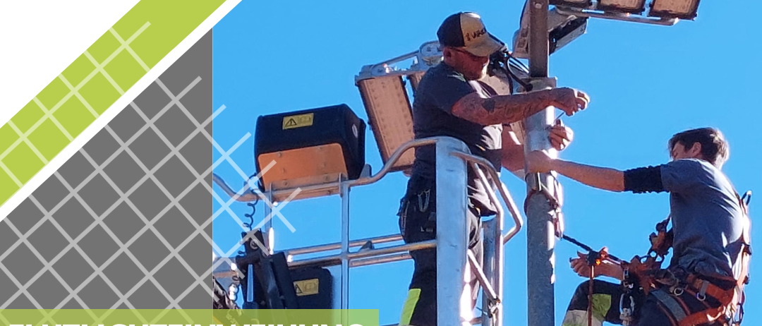 Werbung für eine Flutlichteinweihung am 3. Mai 2025 um 17:00 Uhr. Zwei Arbeiter installieren Flutlichter an einem Metallmast.