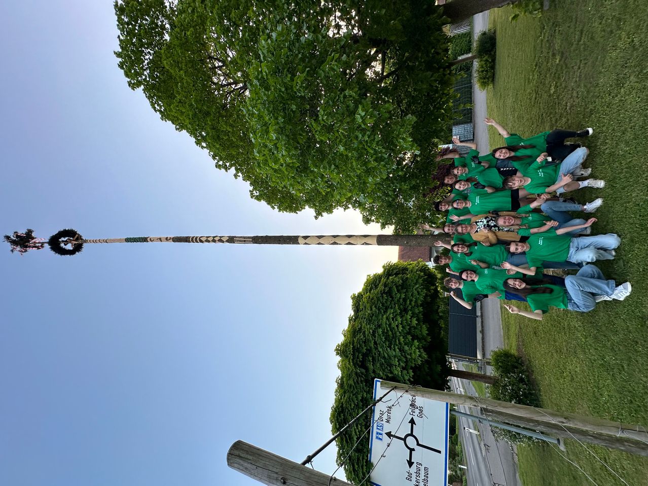 Eine Gruppe von Menschen in grünen T-Shirts posiert für ein Foto in einem Park mit einem hohen Holzpfahl im Hintergrund.