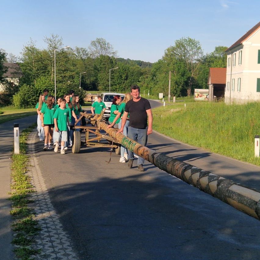 Eine Gruppe von Menschen in grünen Shirts zieht ein langes Objekt mit einem Wagen auf der Straße.