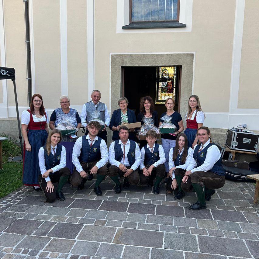 Eine Gruppe von Menschen, einige in traditioneller Kleidung, posiert für ein Foto vor einem Gebäude mit einem Buntglasfenster.