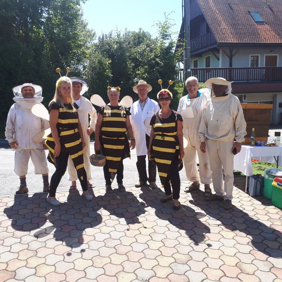 Eine Gruppe von Menschen in Bienenkostümen posiert für ein Foto vor einem Haus mit Bäumen im Hintergrund.