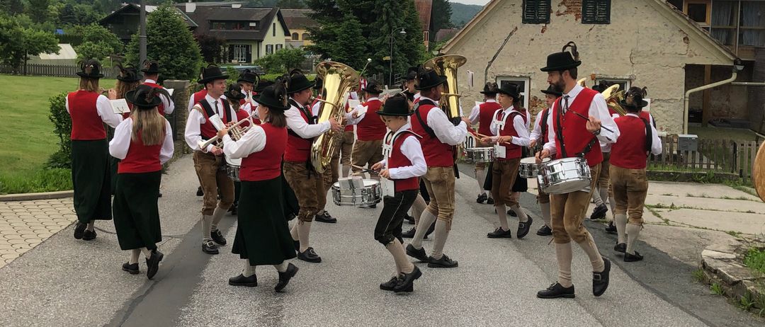 A marching band dressed in traditional attire performs on the street, with members playing trumpets, tubas, and drums.