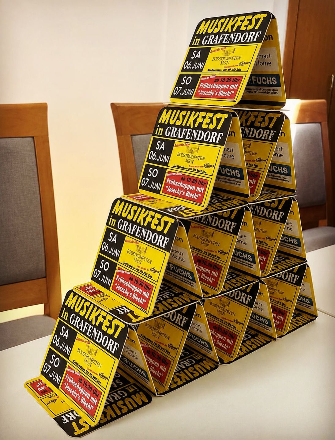 Stacked yellow and red promotional cards for a music festival in Grafendorf, featuring dates and event details on a table.