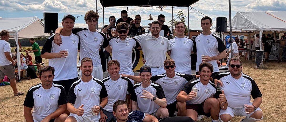 A soccer team poses for a photo in front of a tent with a cloudy sky in the background.