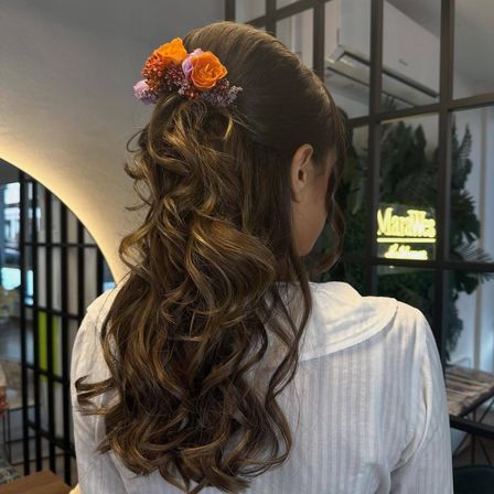 Eine Frau mit lockigem Haar und einer Blumenhaarspange steht vor einem Fenster mit einem Schild, auf dem 'Marques' steht.