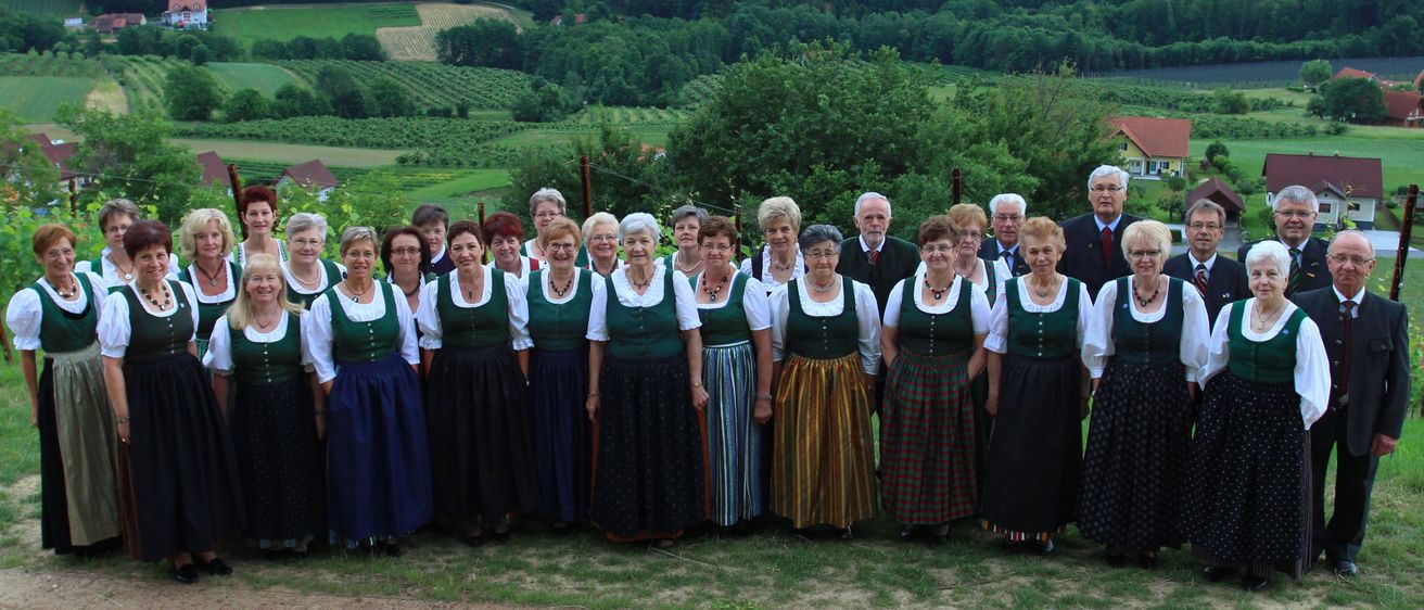 Eine Gruppe älterer Menschen in traditioneller Kleidung posiert für ein Foto in einer malerischen Außenumgebung mit einer Kulisse aus Hügeln und Grünflächen.