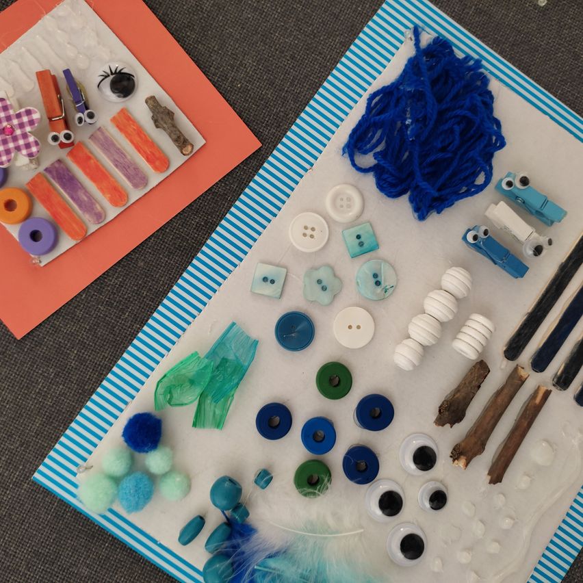 A table with two boards displaying various craft materials. One board has blue yarn, buttons, sticks, and eyes, while the other has a flower, pegs, and more.