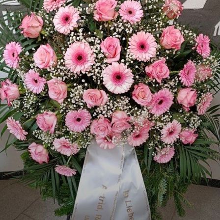 Ein großer Strauß aus rosa Rosen und Gänseblümchen mit einer weißen Schleife, die 'In lieber Erinnerung' steht. Der Strauß ist mit Babysate und grünen Blättern arrangiert.