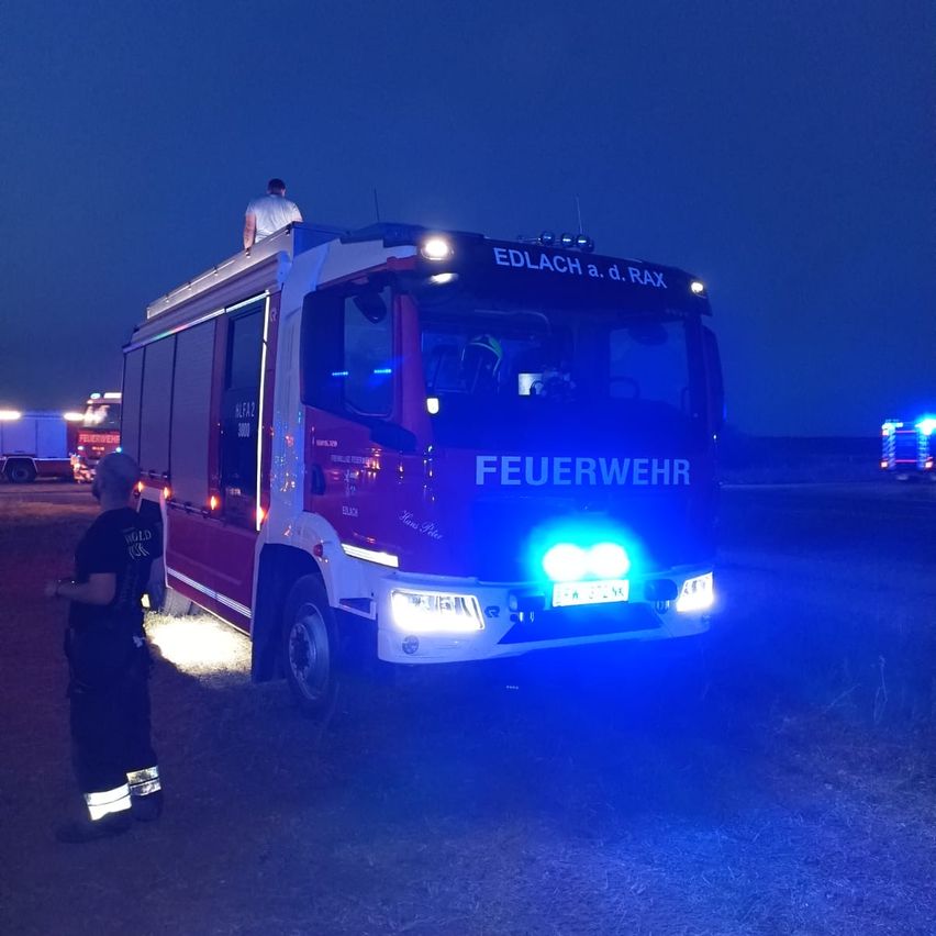Ein Feuerwehrauto mit blinkenden blauen Lichtern steht nachts geparkt, ein Feuerwehrmann steht in der Nähe und einer oben.