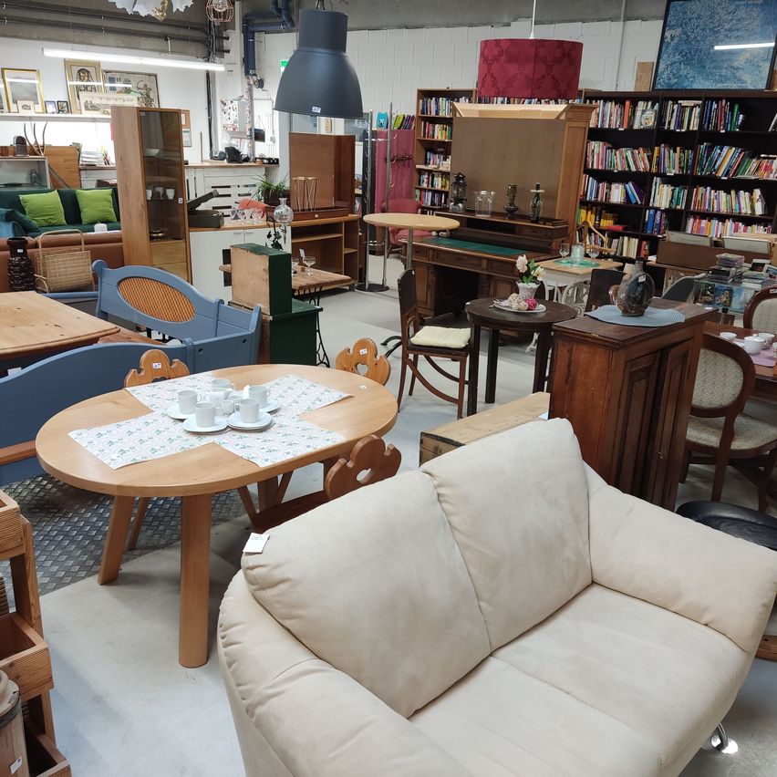 Ein Möbelgeschäft mit runden Tischen, Stühlen und Sofas aus Holz. Ein runder Tisch hat Tassen und Untertassen darauf. Ein Schrank und ein Bücherregal befinden sich im Hintergrund.