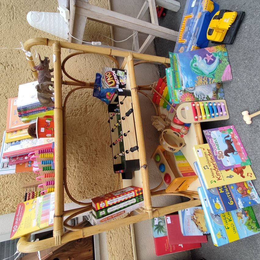 Ein Bambusregal zeigt verschiedene Spielzeuge, Bücher und Lernmaterialien. Gegenstände umfassen eine Tischfußballplatte, Bücher, Puzzles, einen Spielzeughammer und einen Spielzeugdinosaurier.