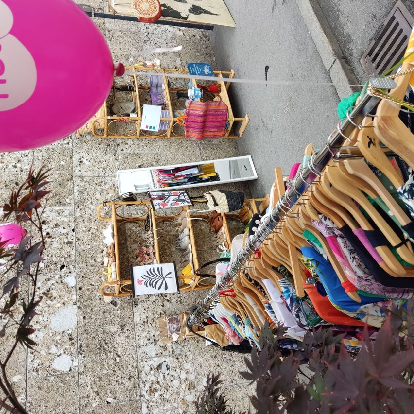 Ein Blick von oben auf einen Markt mit einem rosa Ball, gewebten Körben und verschiedenen ausgestellten Artikeln, einschließlich Kleidung an Kleiderbügeln.