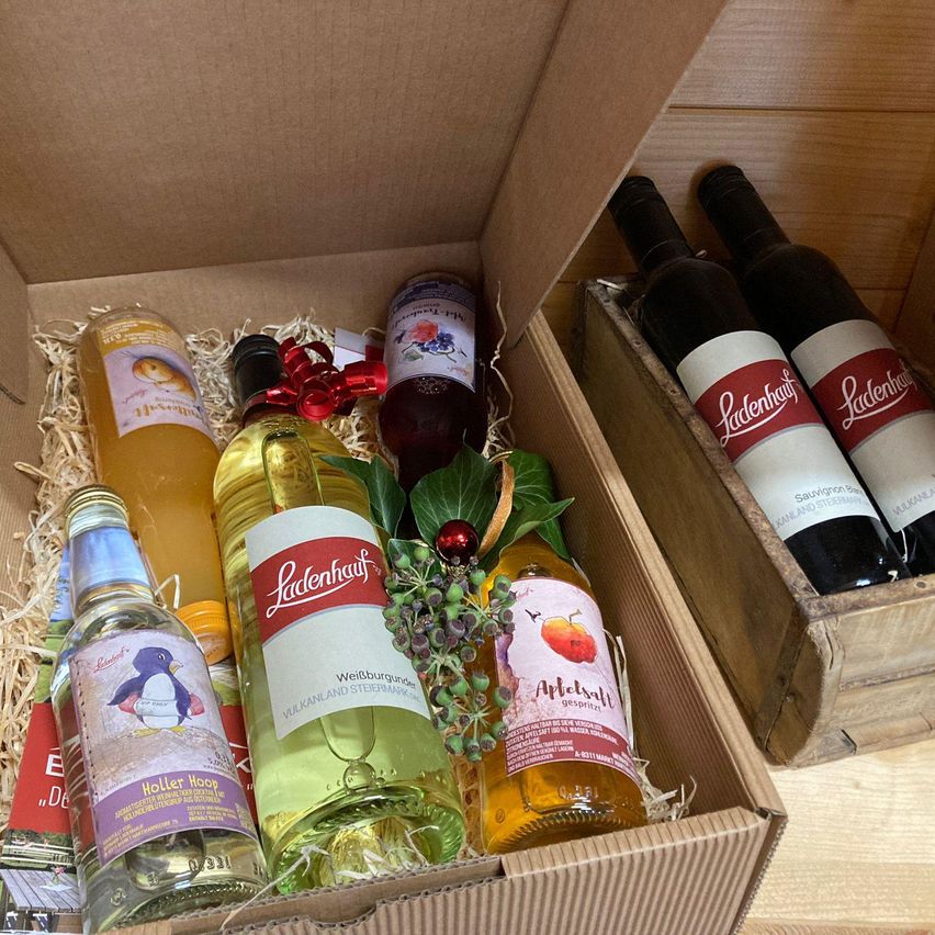 Eine Box enthält verschiedene Flaschen von Ladenhaaf-Produkten, einschließlich Weißwein, Sekt und Apfelwein, mit Feiertagsdekorationen und einer roten Schleife.