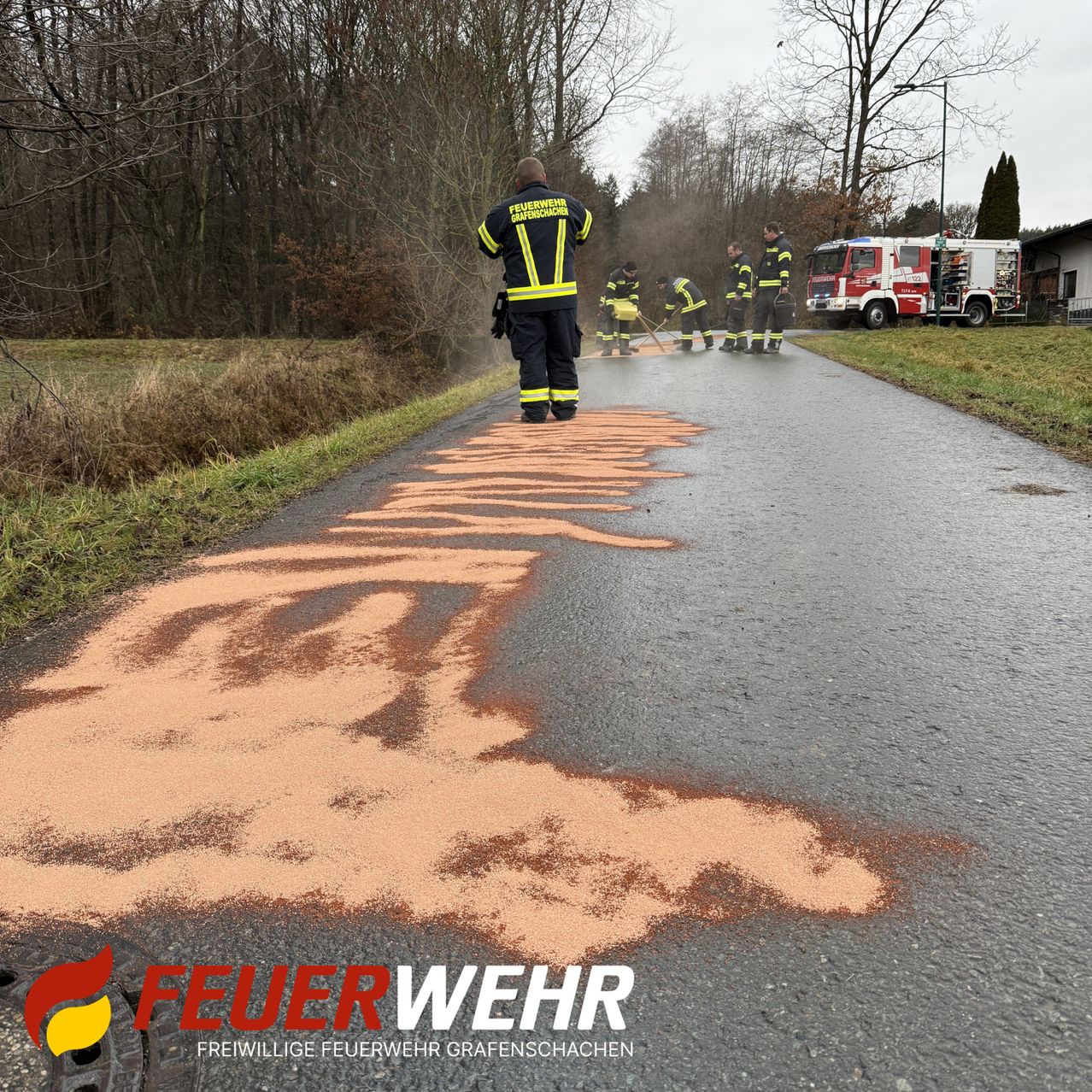 Freiwillige Feuerwehrleute markieren die Straße mit orangefarbenem Pulver, während andere neben einem Feuerwehrwagen stehen.