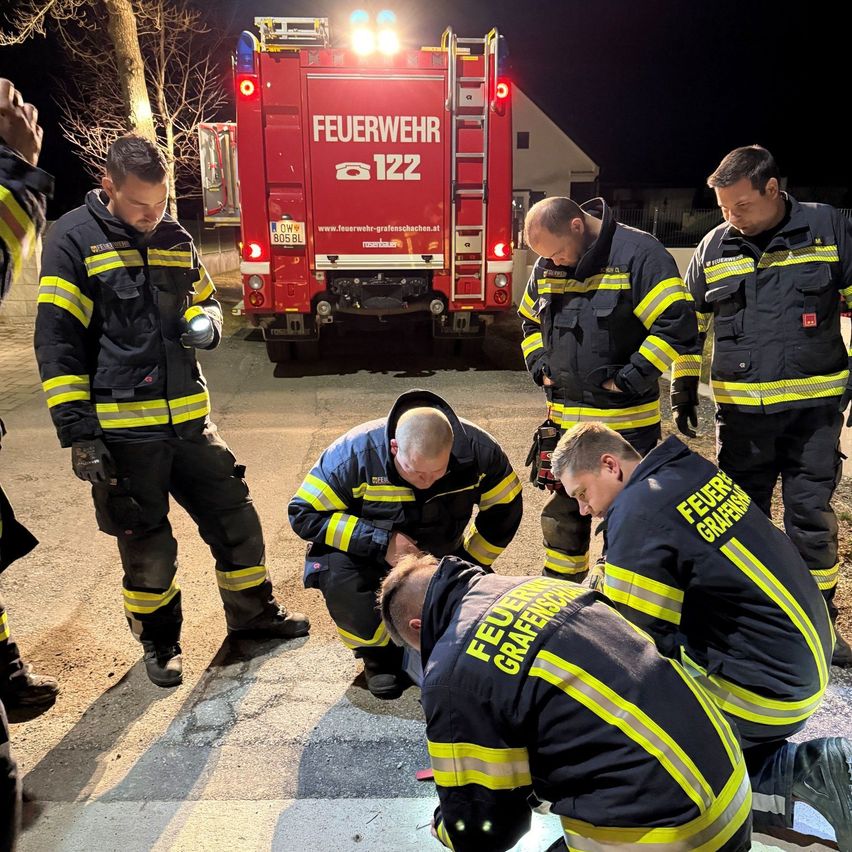 A group of firefighters are attending to an injured person on a street at night with a fire truck in the background.