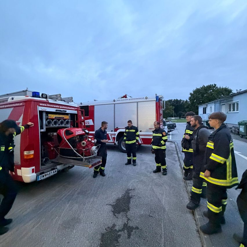 A group of firefighters are gathered around a fire truck, with one man inspecting equipment in the back.