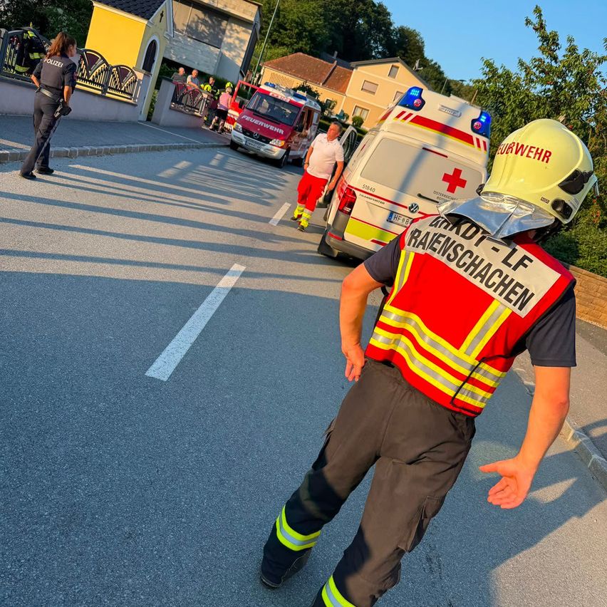Rettungskräfte und Polizei an einem Unfallort. Ein Feuerwehrmann und ein Polizeibeamter stehen in der Nähe eines Feuerwehrwagens und eines Rettungswagens.