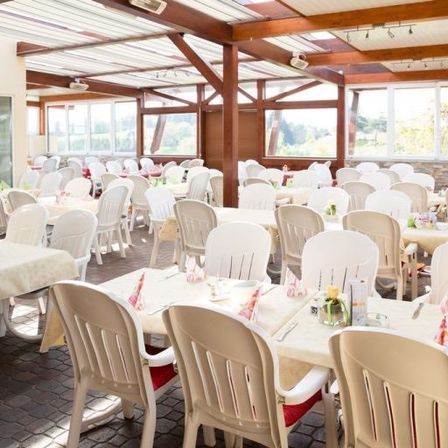 Ein Außenbereich zum Essen mit Tischen und Stühlen, geschmückt mit Tischdecken und Blumen. Die Decke besteht aus Metallplatten und die Wände aus Glas.