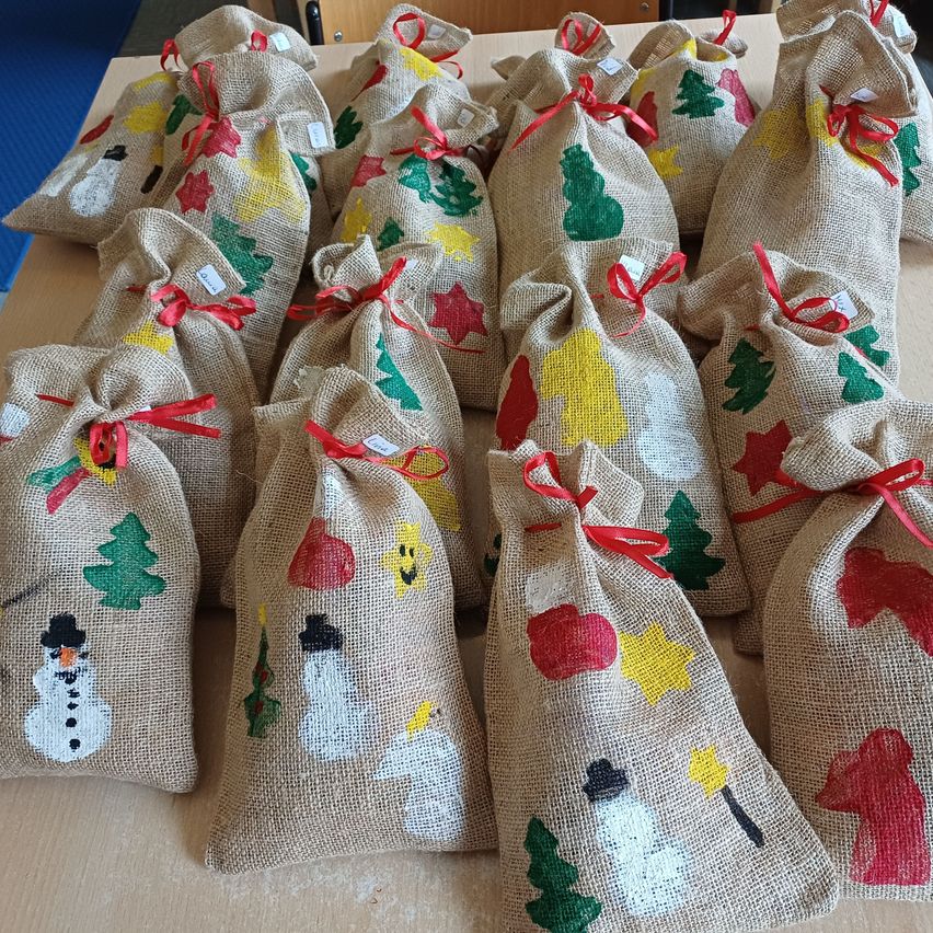 Eine Sammlung von handgefertigten Jutebeuteln mit Weihnachtsdekorationen, darunter Bäume, Sterne und Schneemänner, mit roten Bändern gebunden. Jeder Beutel hat ein einzigartiges Design.