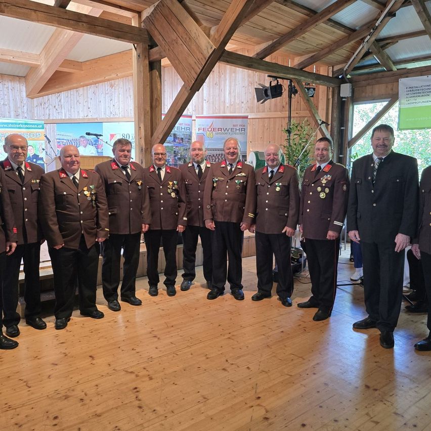 Eine Gruppe von Männern in Uniformen steht in einem Saal, möglicherweise für eine formelle Veranstaltung. Sie tragen Medaillen an ihren Uniformen.