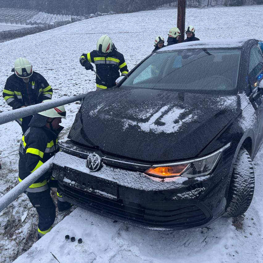 Ein Team von Feuerwehrleuten in gelben und schwarzen Uniformen mit Helmen arbeitet an einem schwarzen Auto auf einem verschneiten Feld. Sie versuchen, es mit Metallstangen zu bewegen.