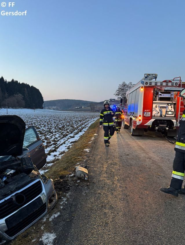 Firefighters are attending to an accident scene on a snowy road with a damaged car and a fire truck nearby.