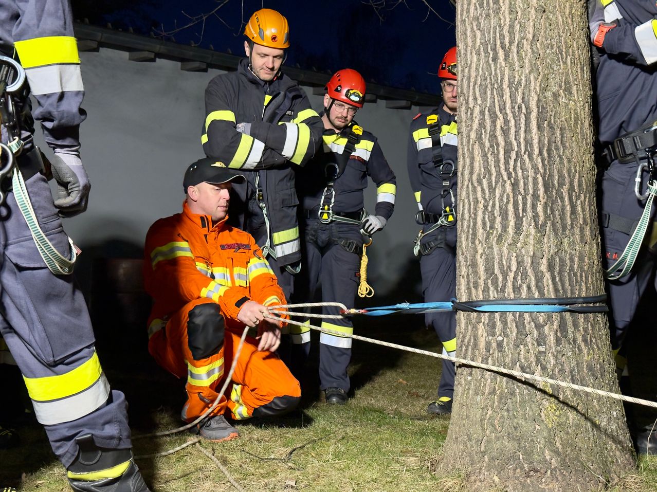 Eine Gruppe von Feuerwehrleuten bereitet sich darauf vor, einen Baum mit Seilen in der Nacht zu fällen. Ein Feuerwehrmann kniet und hält die Seile.