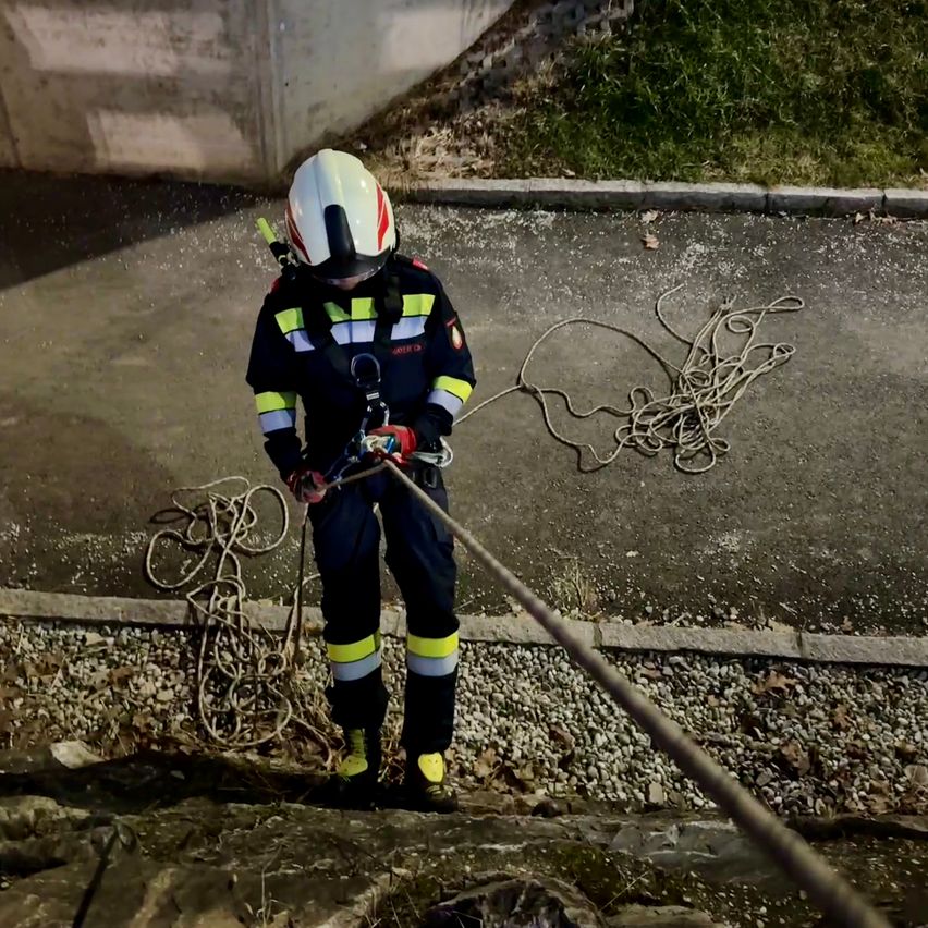 Ein Feuerwehrmann in voller Ausrüstung steht auf einem Bürgersteig und hält ein Seil in der Hand, wahrscheinlich in Vorbereitung auf eine Rettungsaktion.