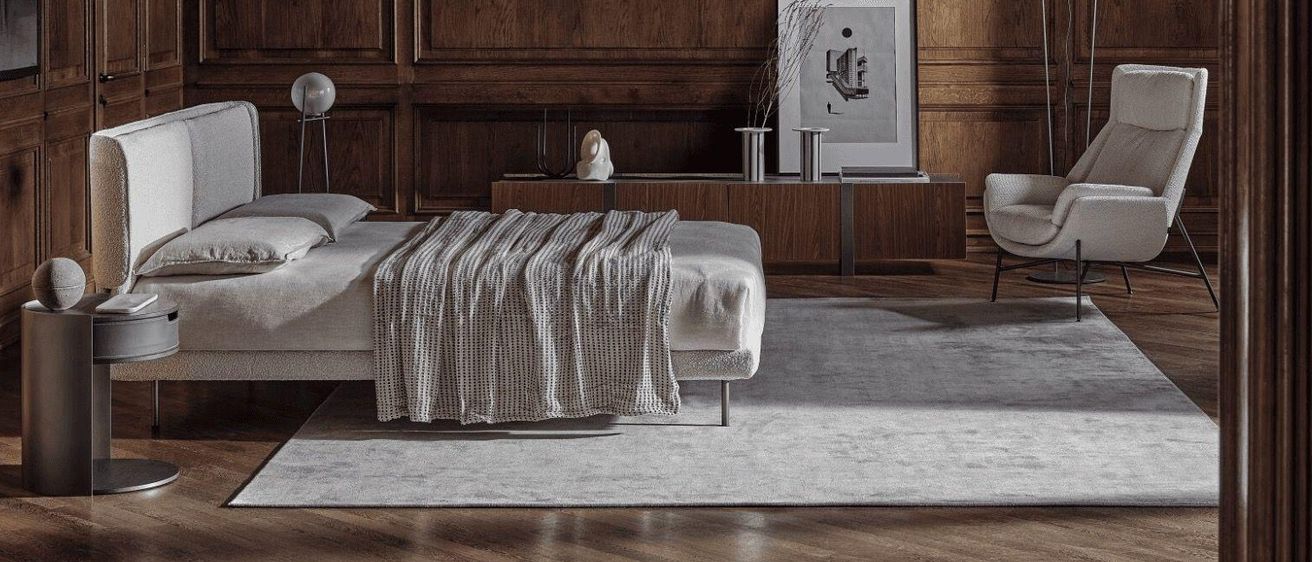 Ein modernes Schlafzimmer mit Holzwänden und einem Bett, das mit einer grauen Decke bedeckt ist, mit einem gerahmten Bild und einer Vase auf einem Holzschrank.