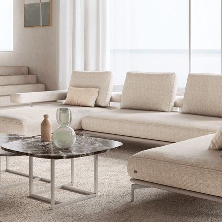 Ein modernes Wohnzimmer mit einem großen weißen Sofa, einem Marmortisch und einer Treppe mit weißen Vorhängen.