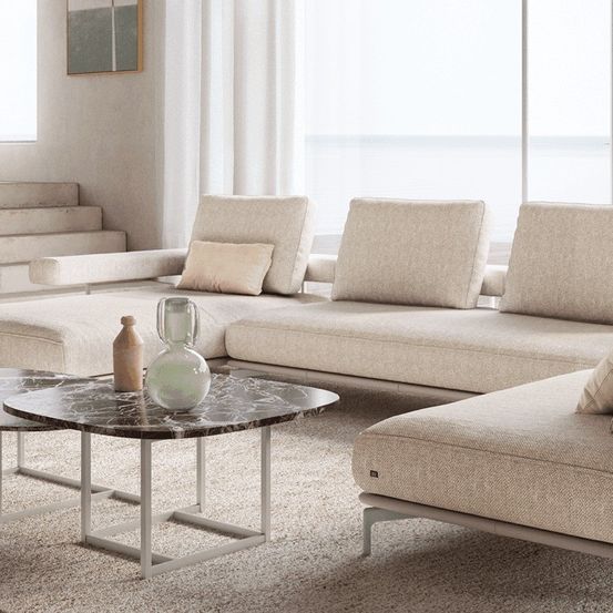 Ein modernes Wohnzimmer mit einem großen weißen Sofa, einem Marmortisch und einer Treppe mit weißen Vorhängen.