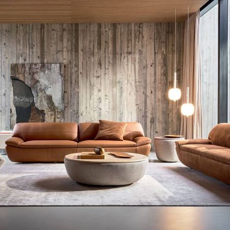 Ein modernes Wohnzimmer mit Holzwänden, zwei braunen Ledersofas, einem runden Couchtisch und hängenden Lampen.