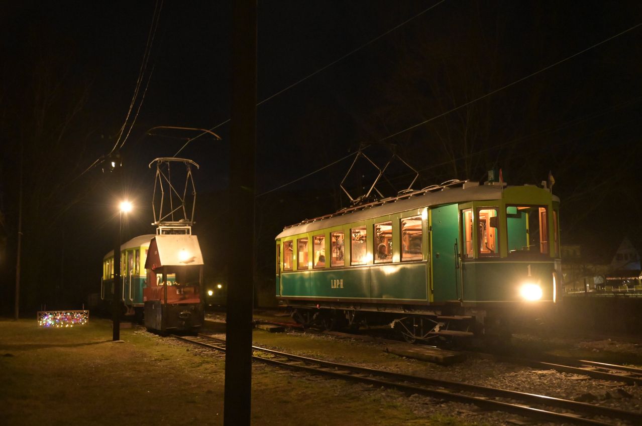 Two green vintage trams are parked at night, one with lit windows, the other with a lit lamp, on a railway track.