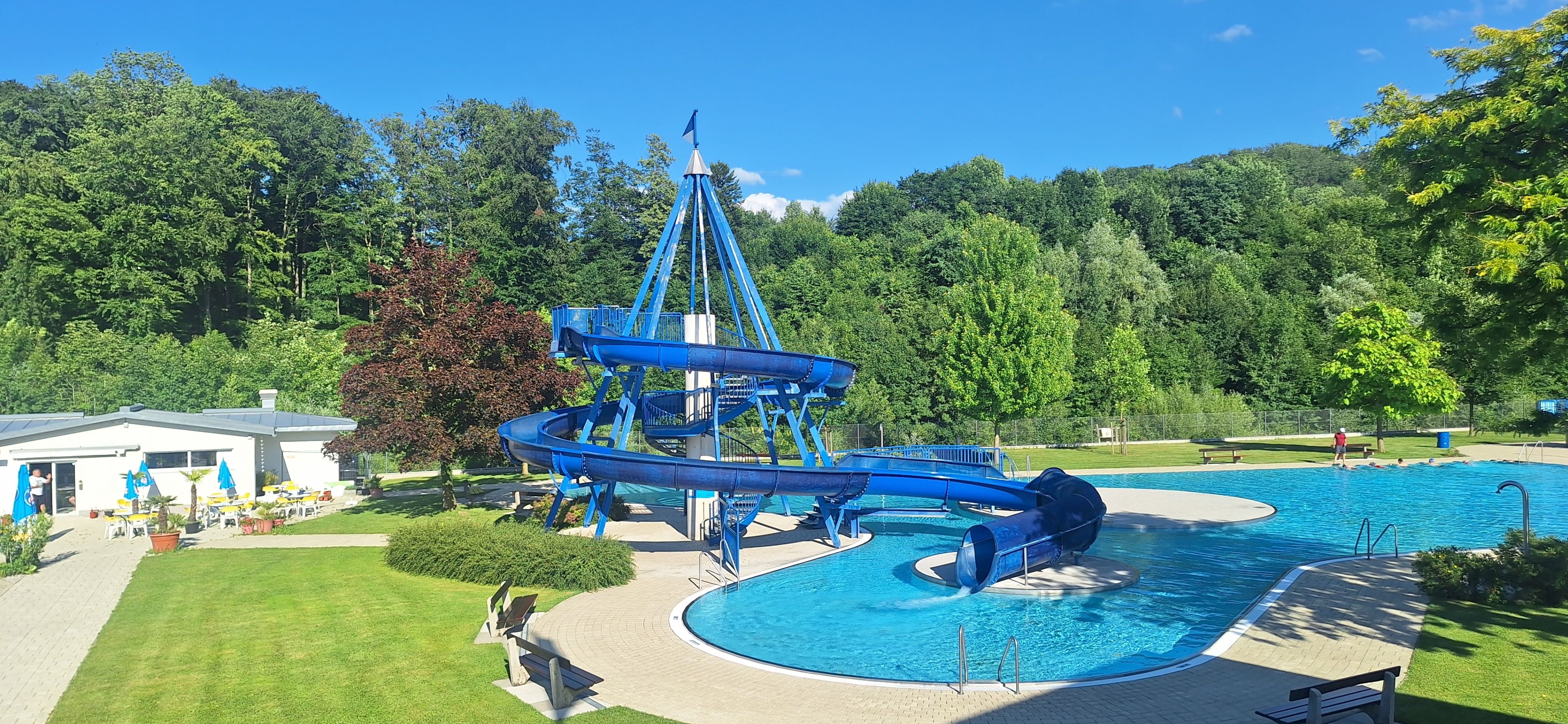 Eine blaue Spiralwasserrutsche befindet sich über einem Schwimmbad mit klarem blauem Himmel im Hintergrund.