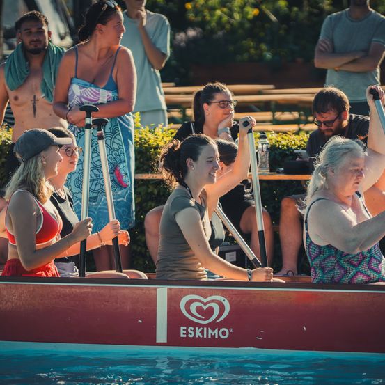 Eine Gruppe von Frauen paddelt ein rotes Eskimo-Boot im Pool, während Zuschauer zusehen.