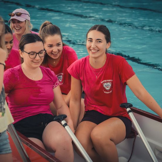 Eine Gruppe von Frauen in roten T-Shirts sitzt in einem Boot, lächelt und posiert für ein Foto im Pool.