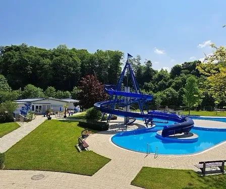 Eine Vogelperspektive auf einen Wasserpark mit einem großen blauen Wasserrutsche, umgeben von grünem Gras und Bäumen.