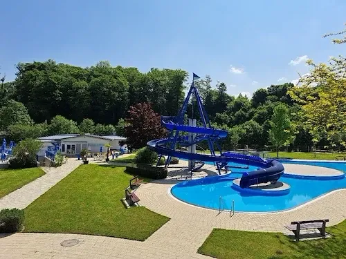 Eine Vogelperspektive auf einen Wasserpark mit einem großen blauen Wasserrutsche, umgeben von grünem Gras und Bäumen.