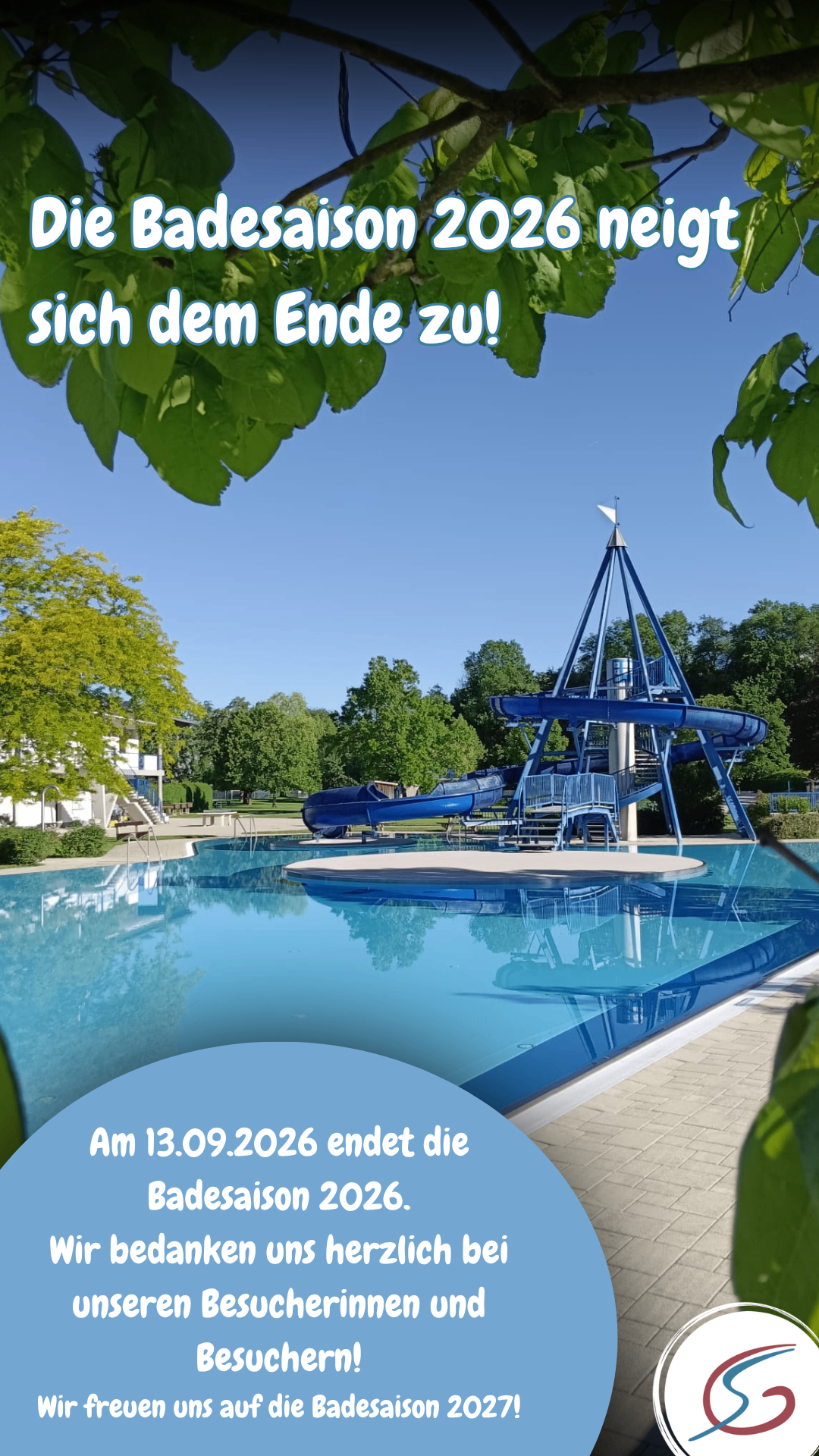 Eine große blaue Wasserrutsche befindet sich in der Mitte eines Schwimmbeckens mit klarem blauem Wasser. Bäume und ein Gebäude sind im Hintergrund. Die Rutsche ist von einem weißen Deck umgeben.