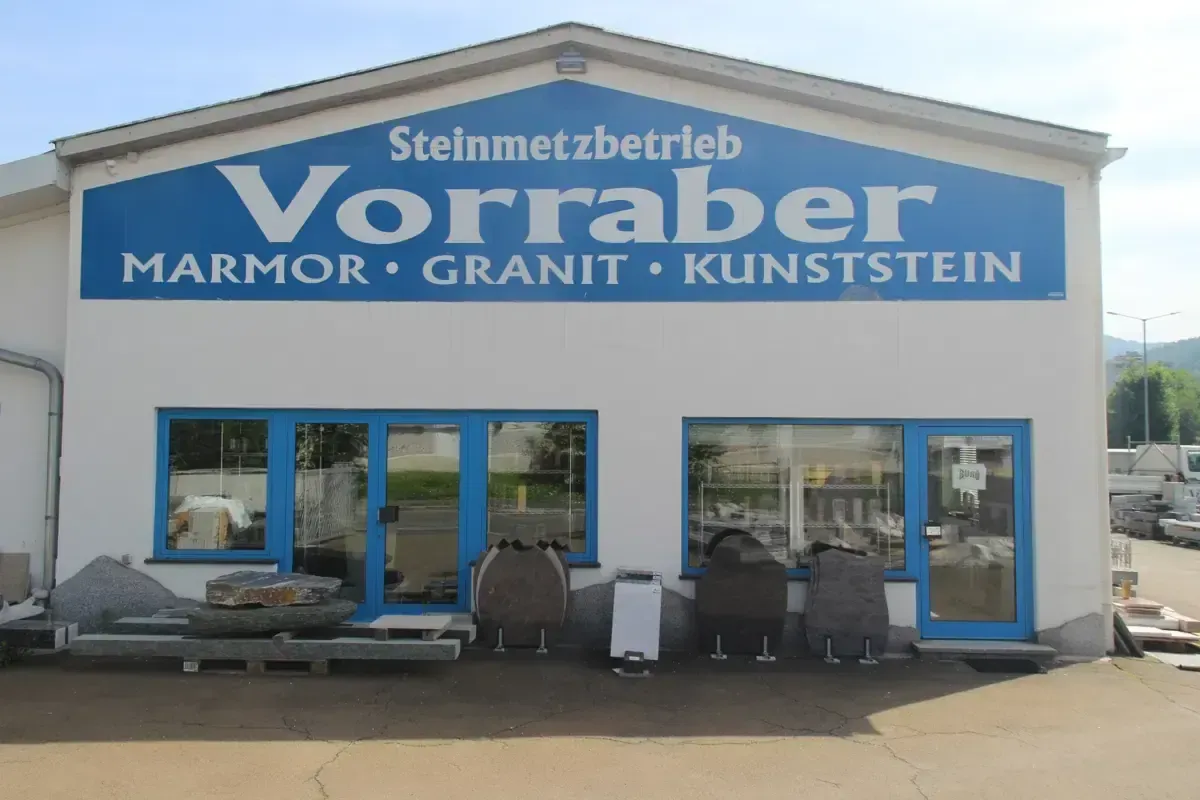 Das Vorraber Steinmetzbetrieb ist spezialisiert auf Panzerung, Granit und Kunststein. Das Geschäft hat blaue Türen, ein großes Schild und Steindisplays draußen.